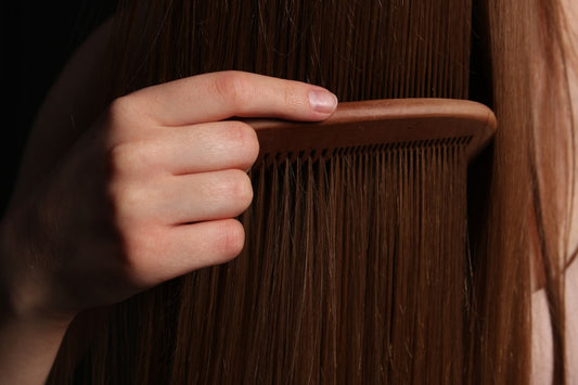 A hand combing through long brown hair, checking for thinning and shedding